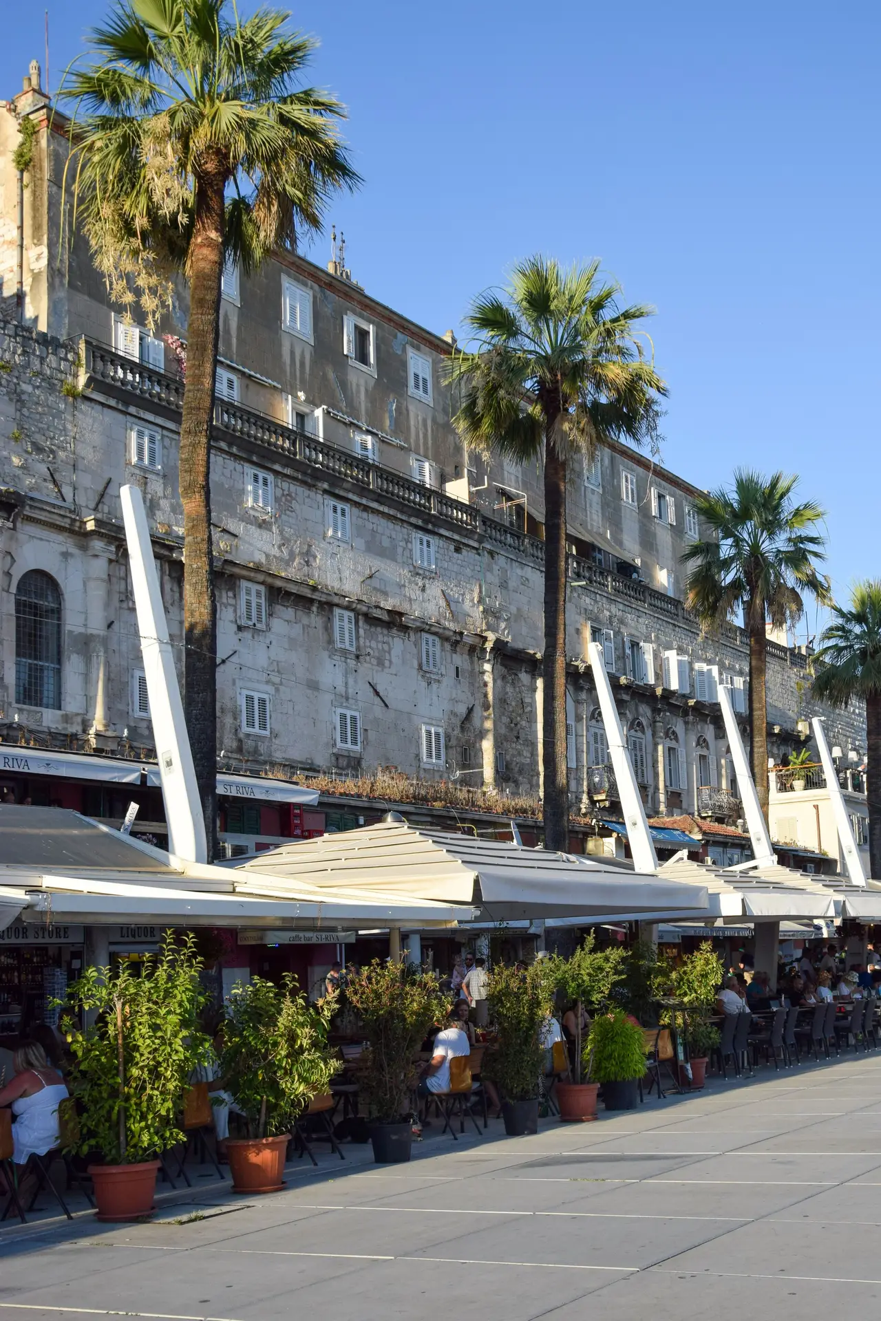 outside terraces with people sitting and wall with palm trees in the background